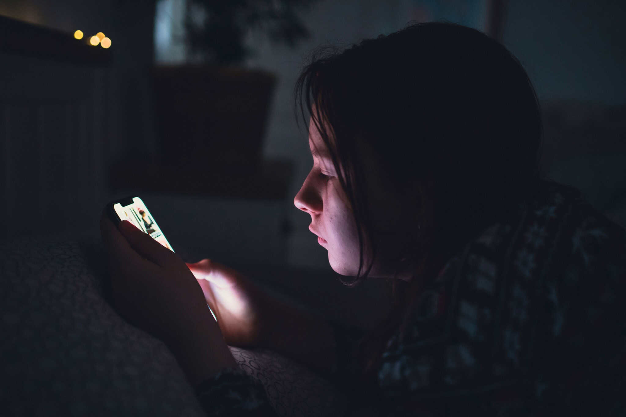 Criança no escuro usando um celular
