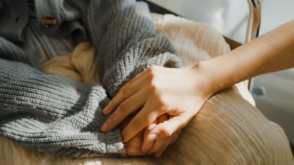 A person holds hands with an ill person with a blanket on their lap (Stock image)