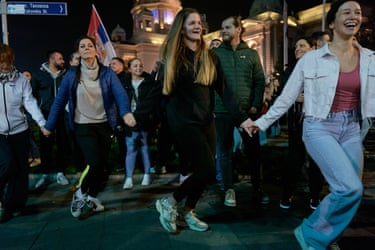 Young women holding hands and dancing amid a crowd in Belgrade